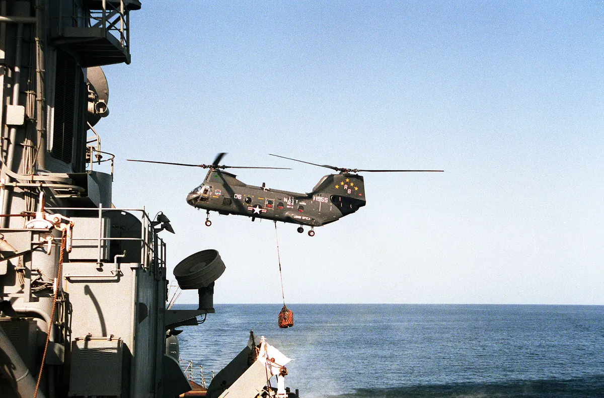 Navy Sea Knight helicopter hovering beside an aircraft carrier