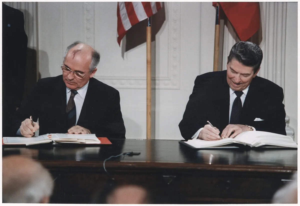 Reagan and Gorbachev seated at a signing table with pens